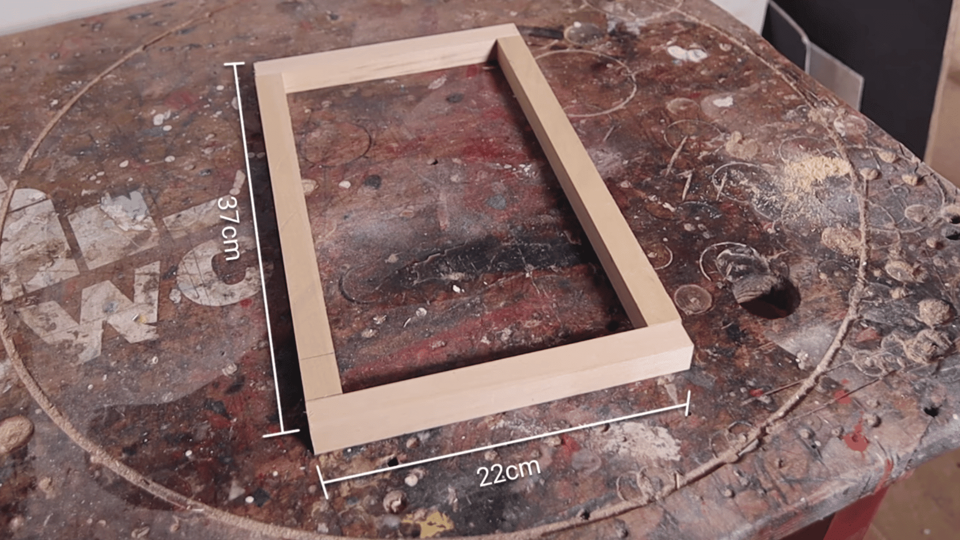 Wooden frame on a workbench labeled 37 cm by 22 cm, showing dimensions for a small weaving loom frame.