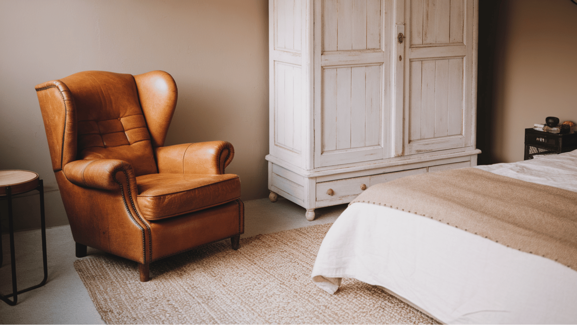 a cozy bedroom featuring a leather armchair and rustic white wardrobe.