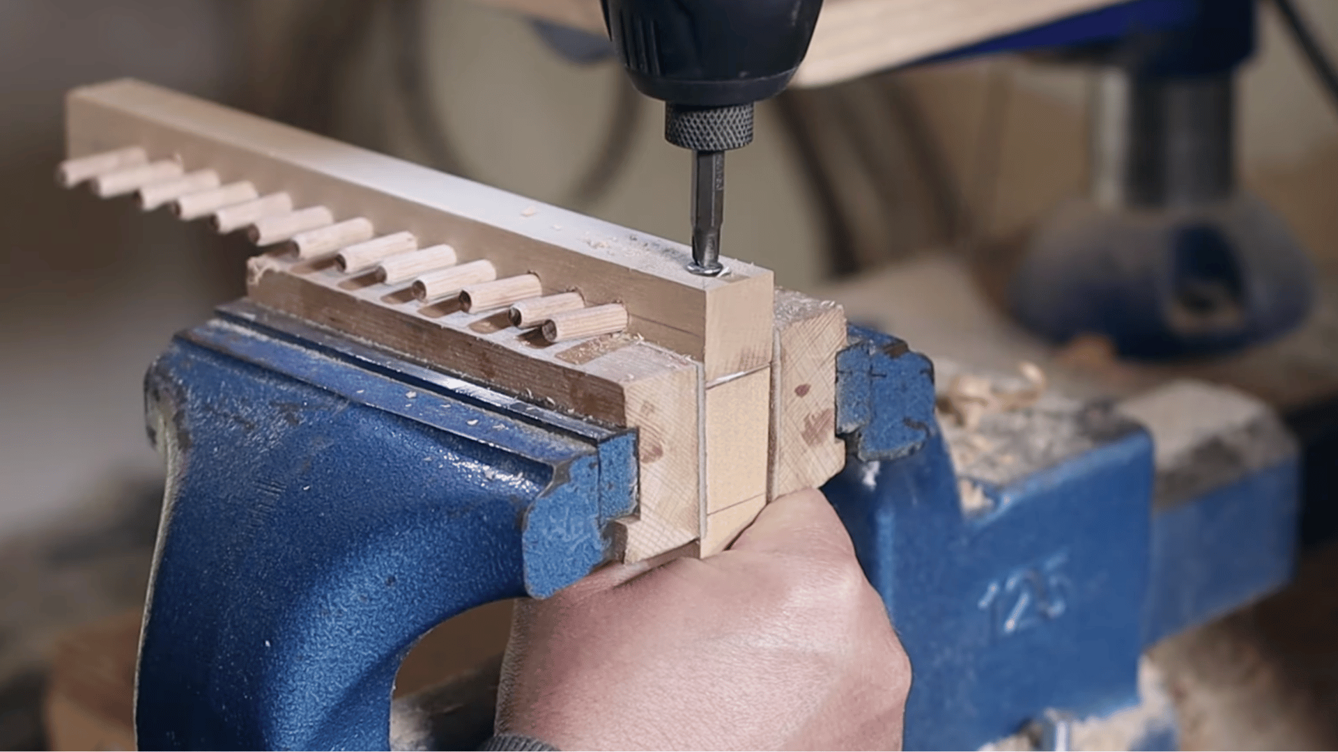 a person drilling holes into the wooden frame for the warp threads on a loom.