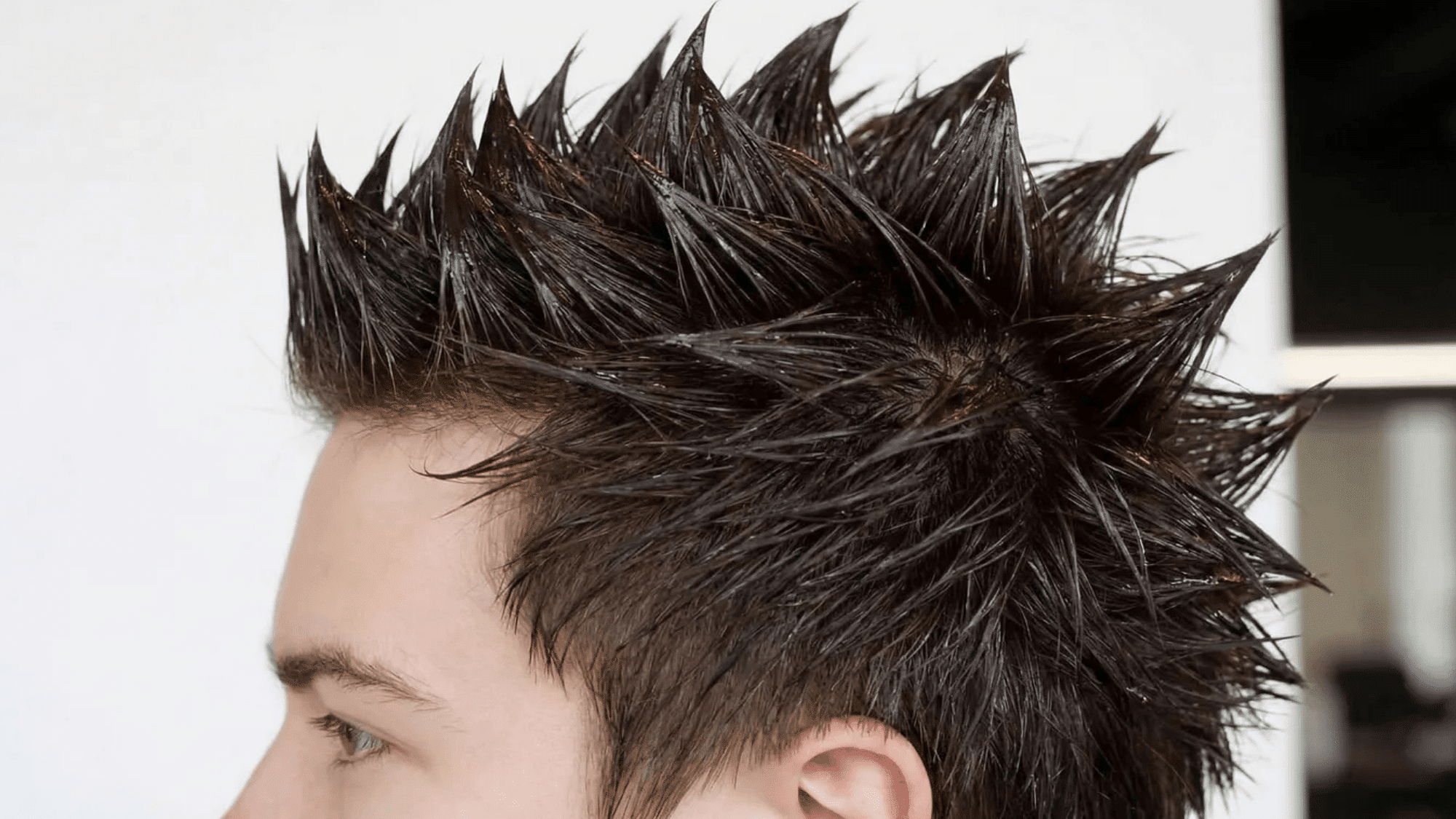 a person with a spiked, gelled hairstyle, featuring sharp, spiked tips, against a neutral background