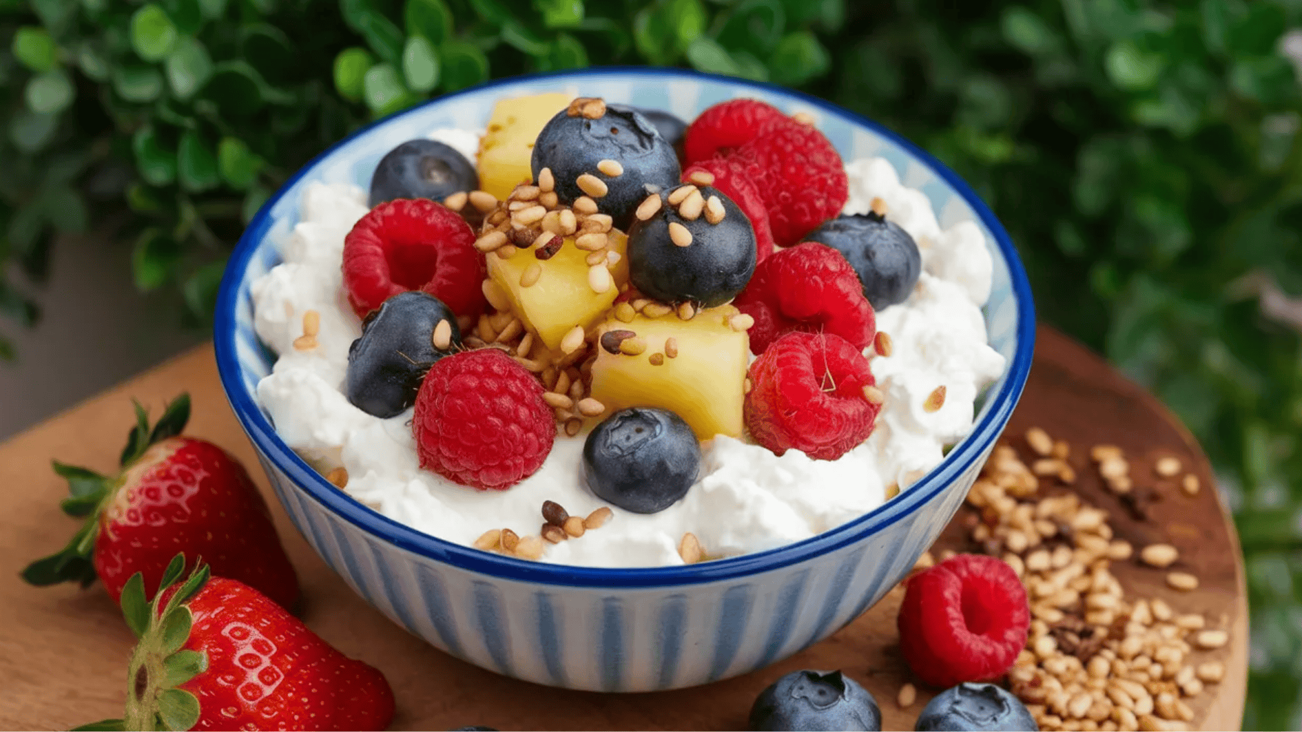 bowl of cottage cheese topped with raspberries, blueberries, pineapple, and sunflower seeds, with strawberries on the side