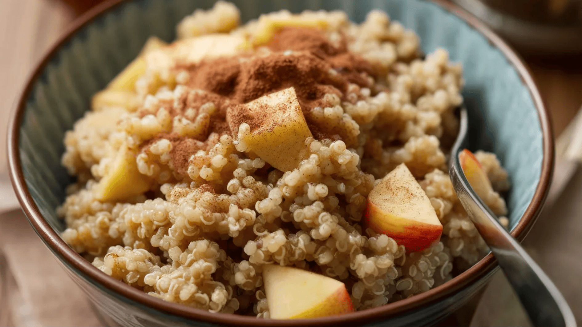 bowl of quinoa topped with diced apples and a sprinkle of cinnamon, served with a spoon on the side