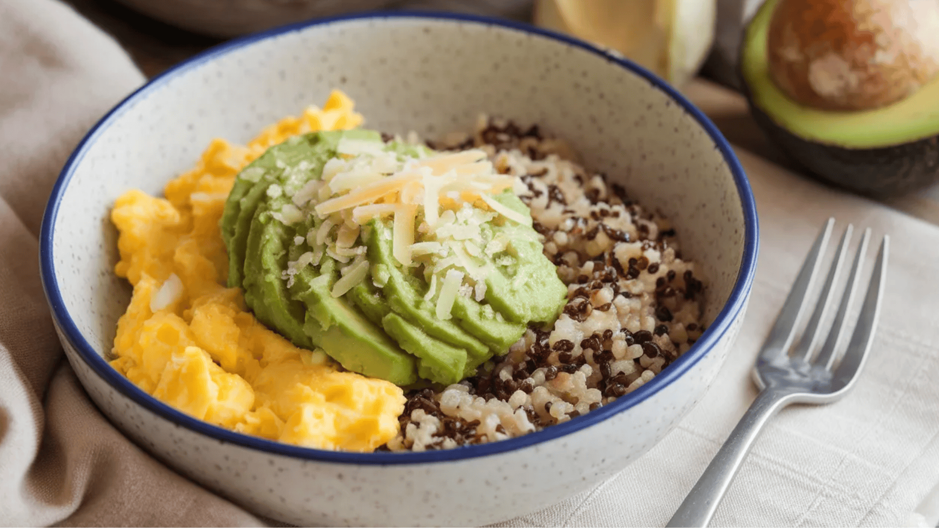 bowl with scrambled eggs, quinoa, sliced avocado, and grated cheese, served with a silver fork on the side