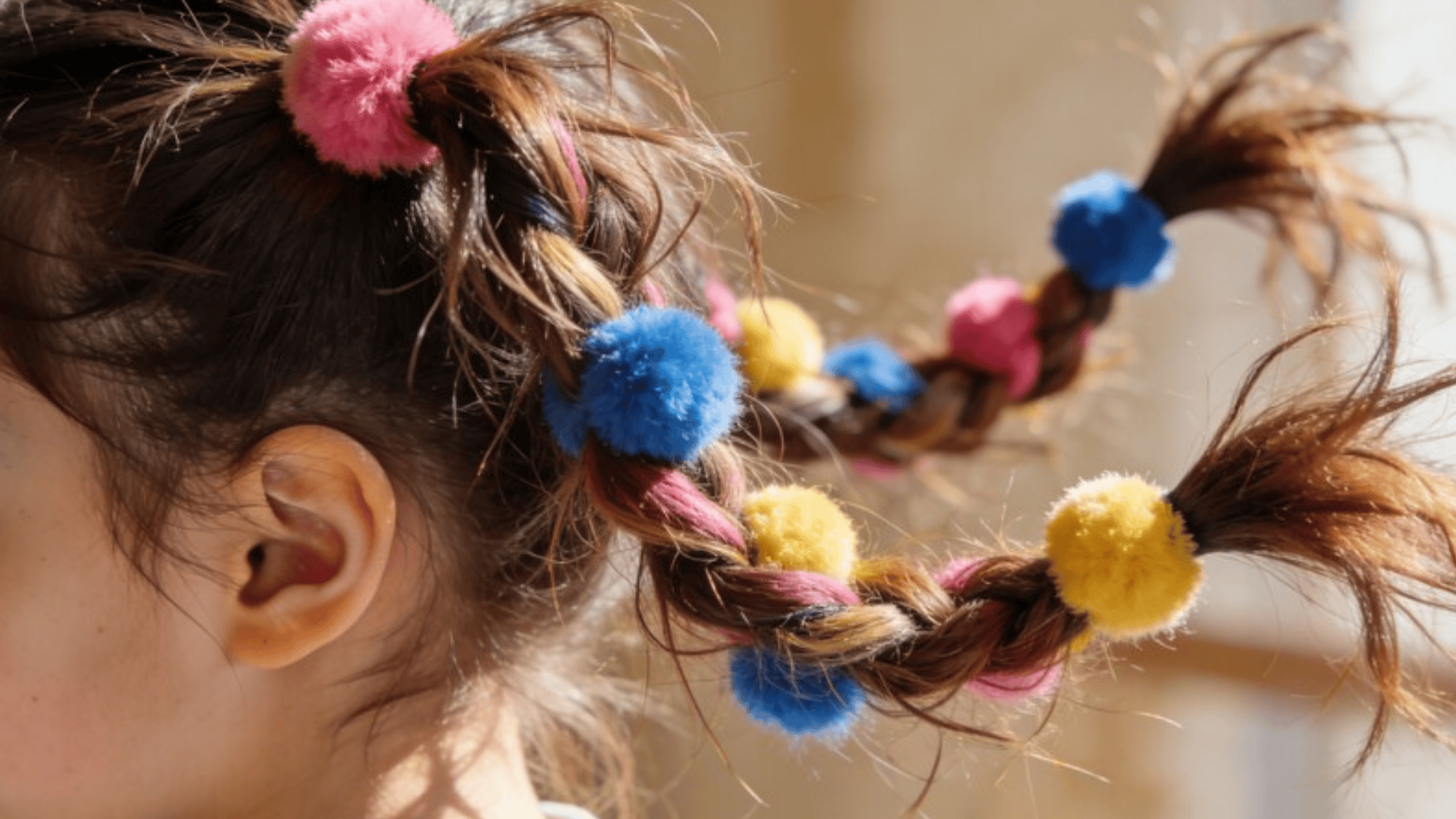 bright and colorful braided pigtails adorned with fluffy pink, blue, and yellow pom-poms, creating a playful hairstyle