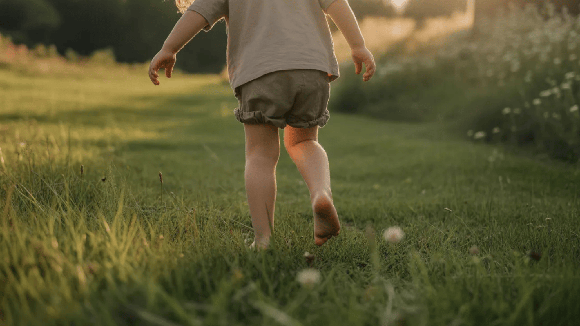 child walking barefoot on grass in a garden