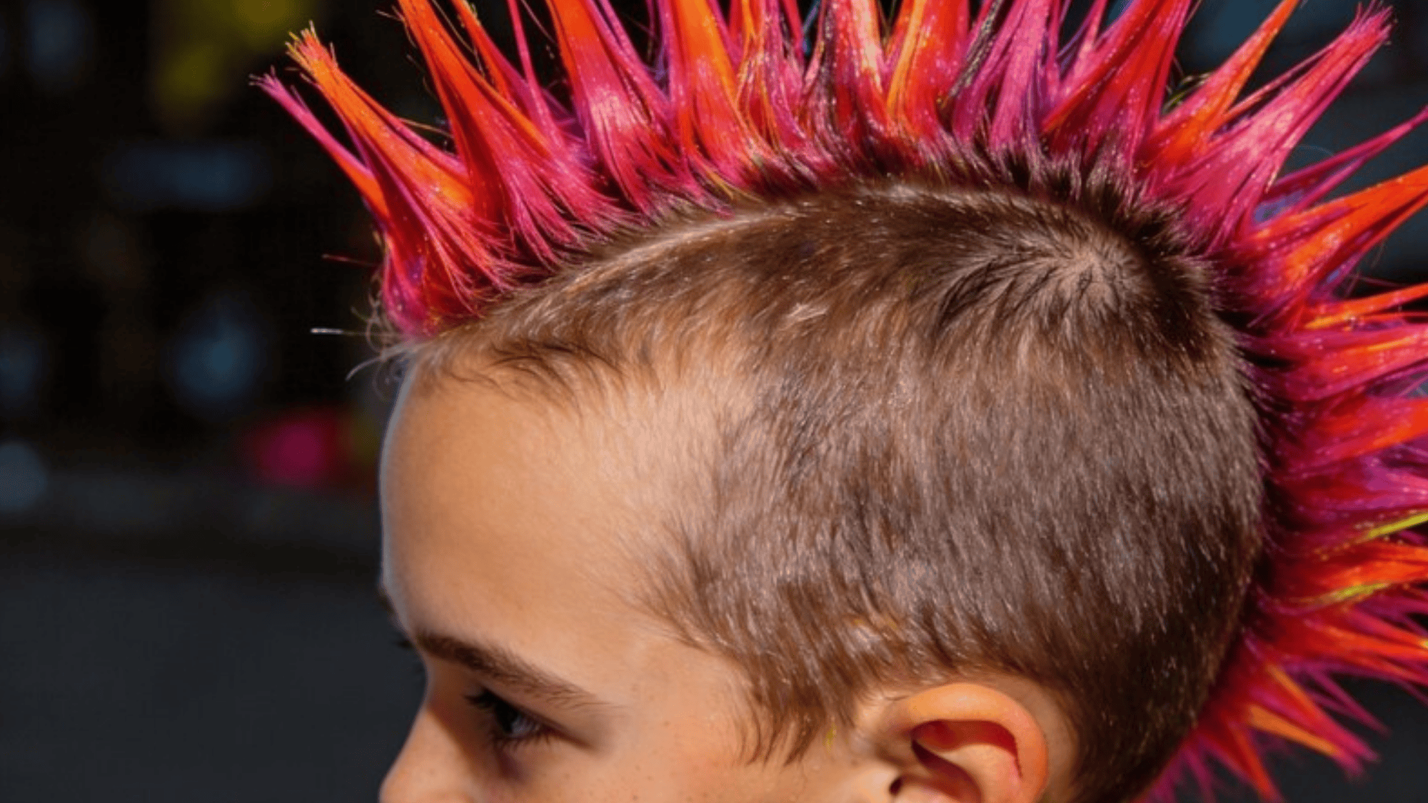 child with a vibrant, spiky mohawk hairstyle featuring shades of pink, orange, and yellow