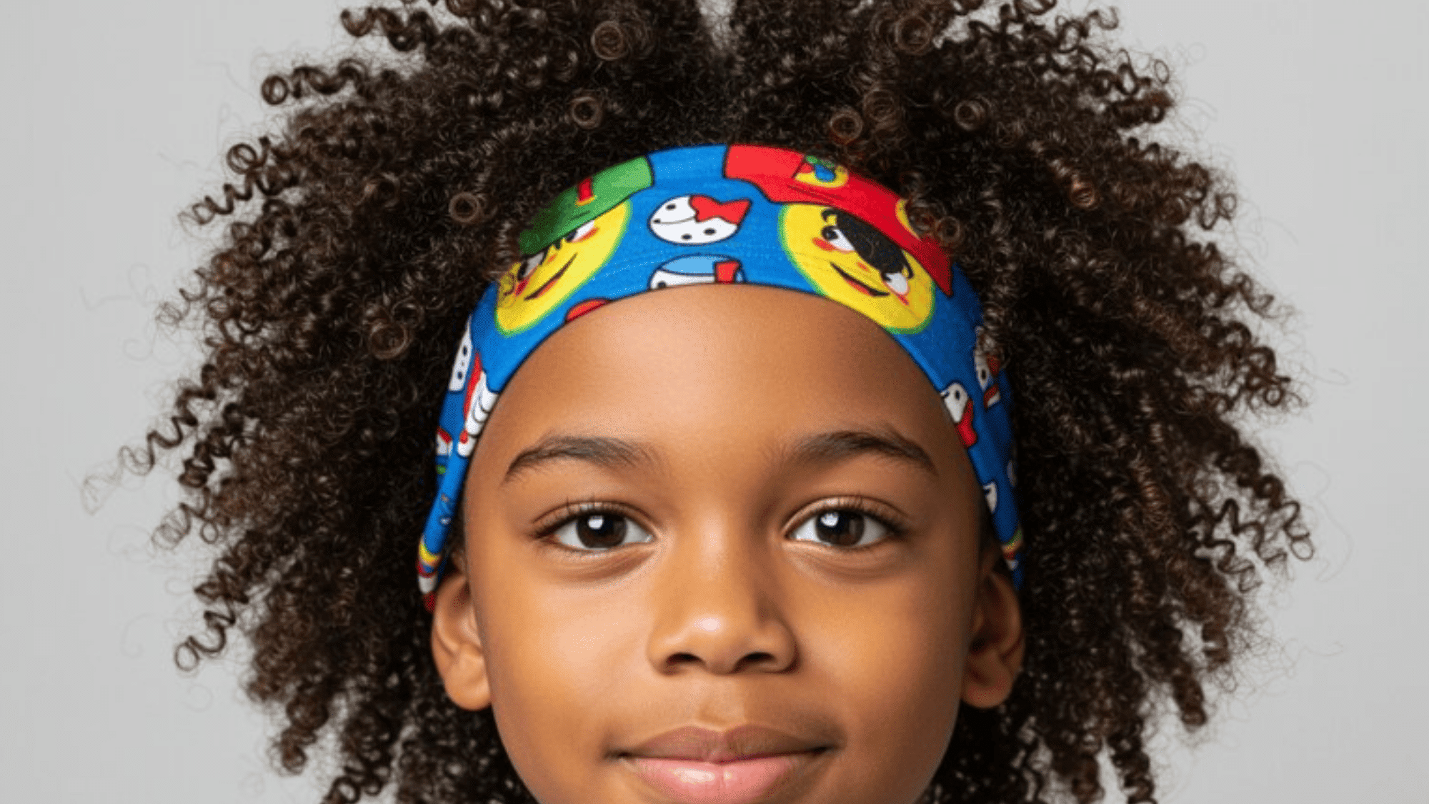 child with curly hair wearing a colorful cartoon-patterned headband, smiling softly for the camera