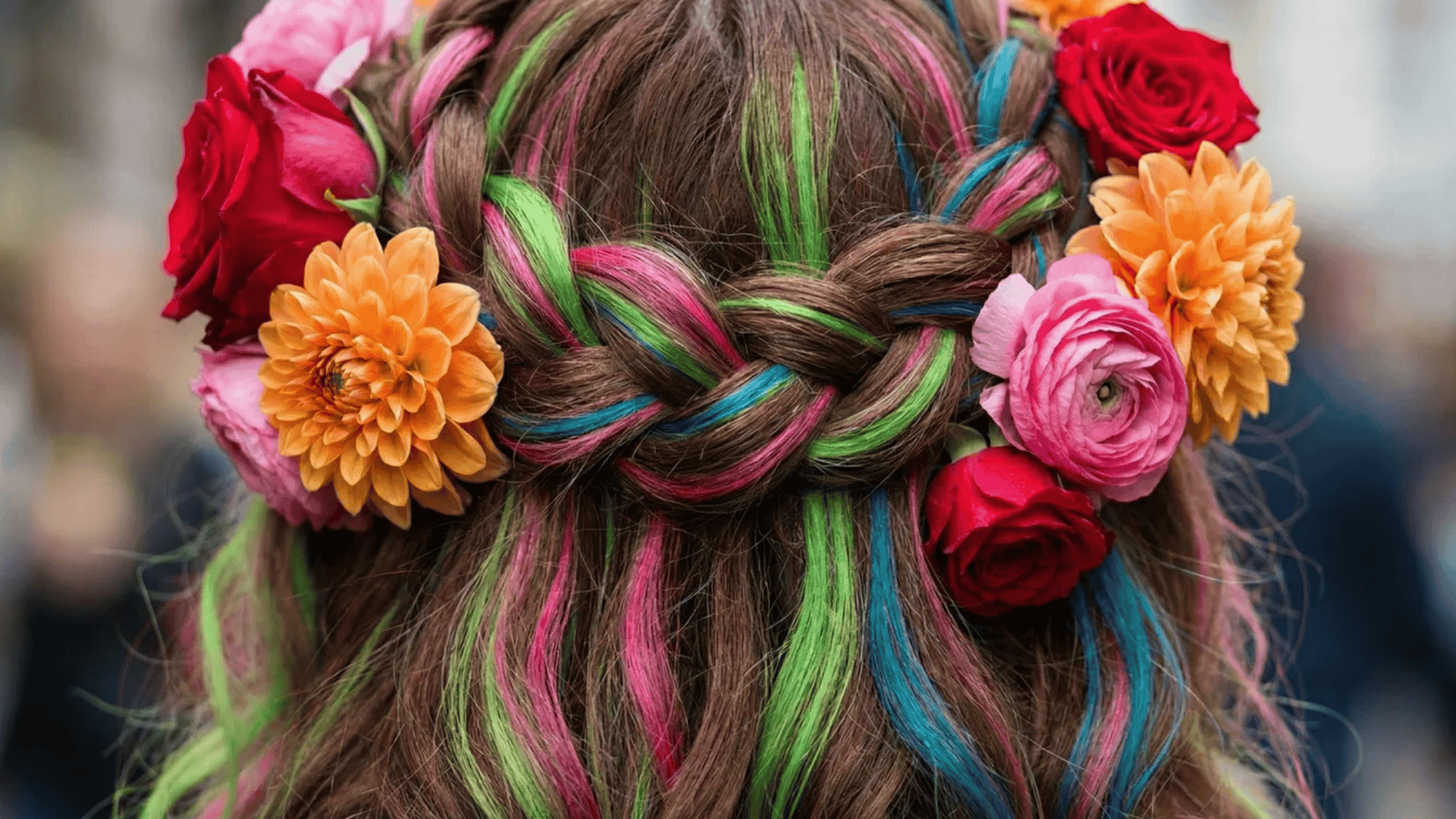 colorful braided hairstyle with pink, green, and blue streaks, adorned with red, pink, and orange flowers for a vibrant and festive look