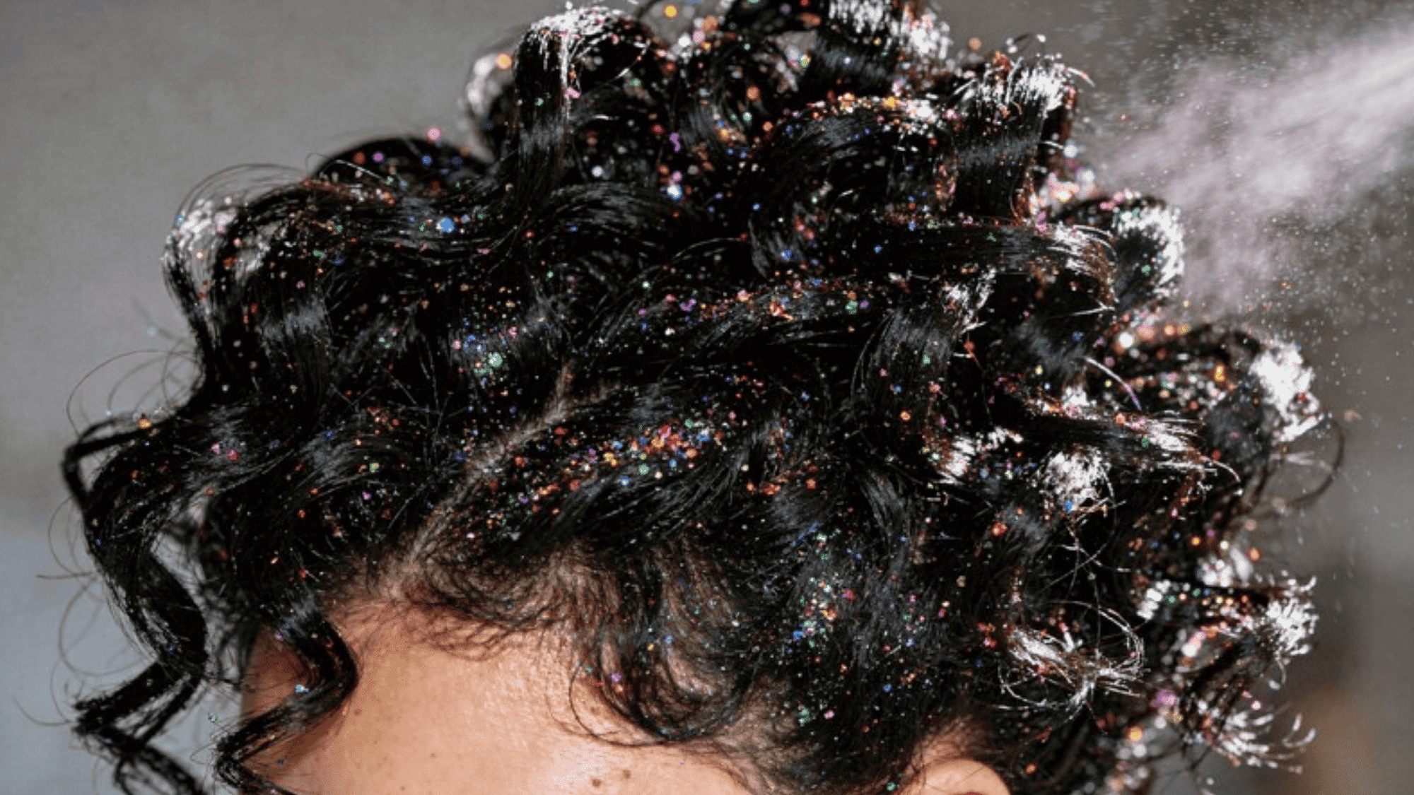 curly hair adorned with shimmering glitter, giving a playful, sparkly effect as hair spray is applied