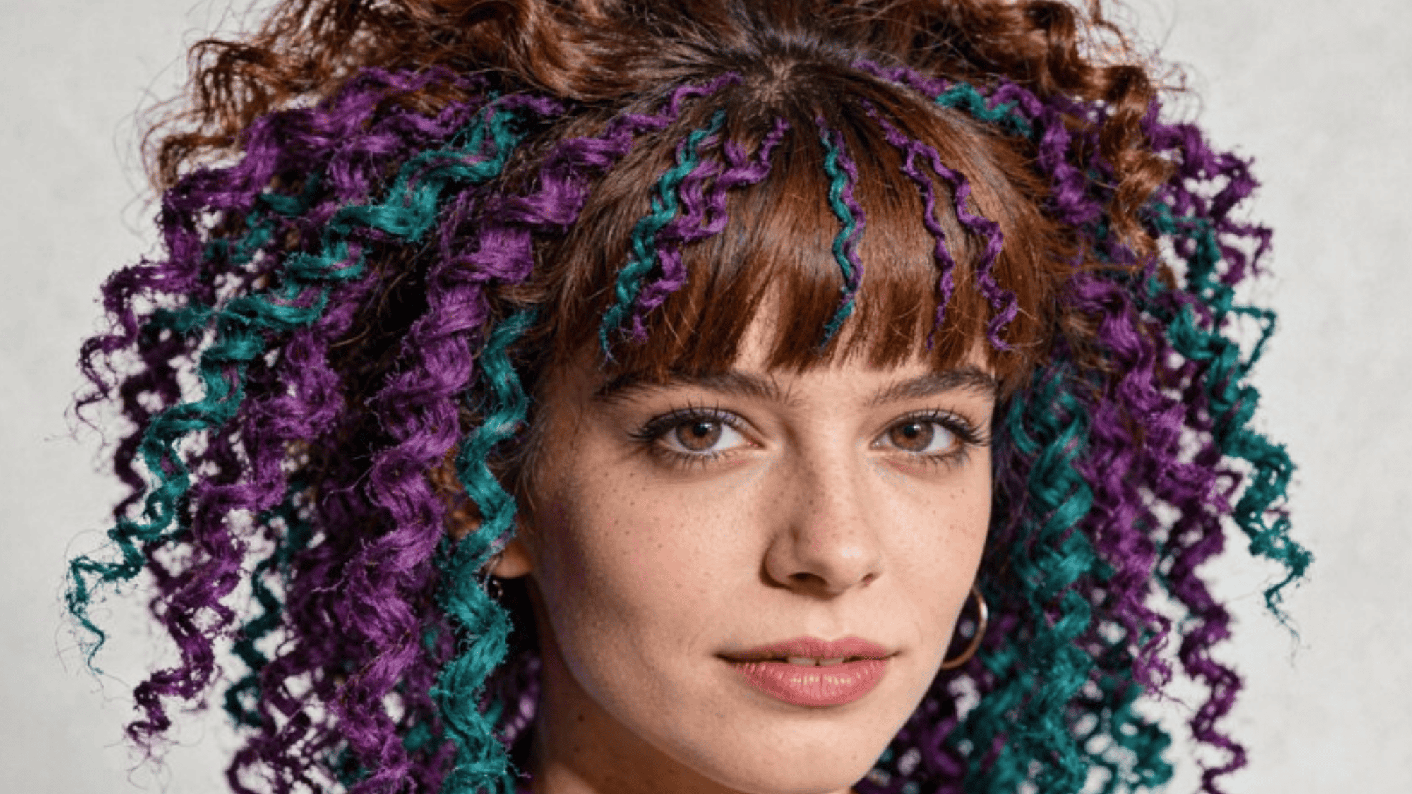 curly hair with vibrant purple and teal streaks, paired with bangs, creating a bold and colorful hairstyle
