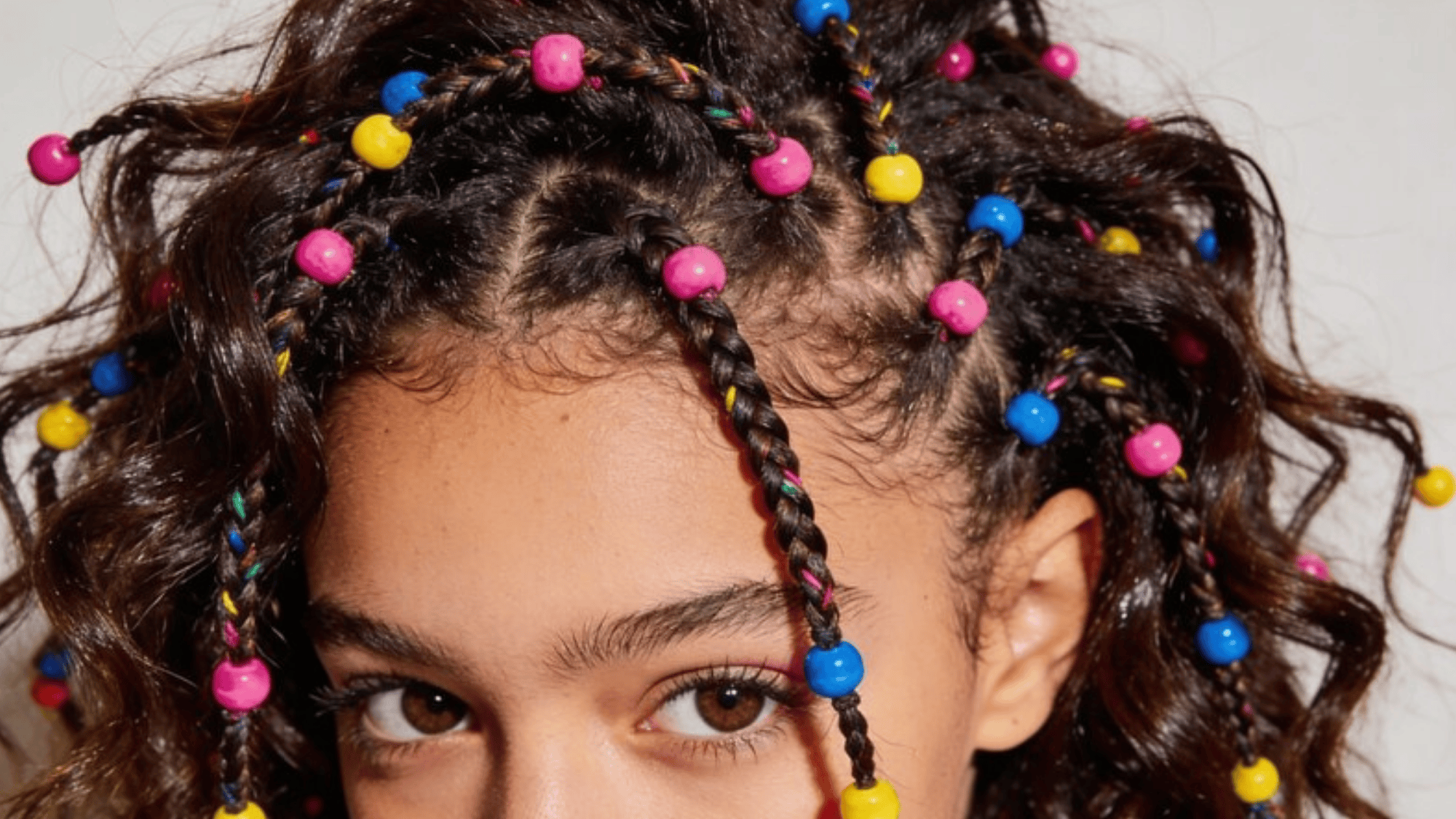 girl with curly hair styled in colorful braids adorned with vibrant pink, blue, and yellow beads