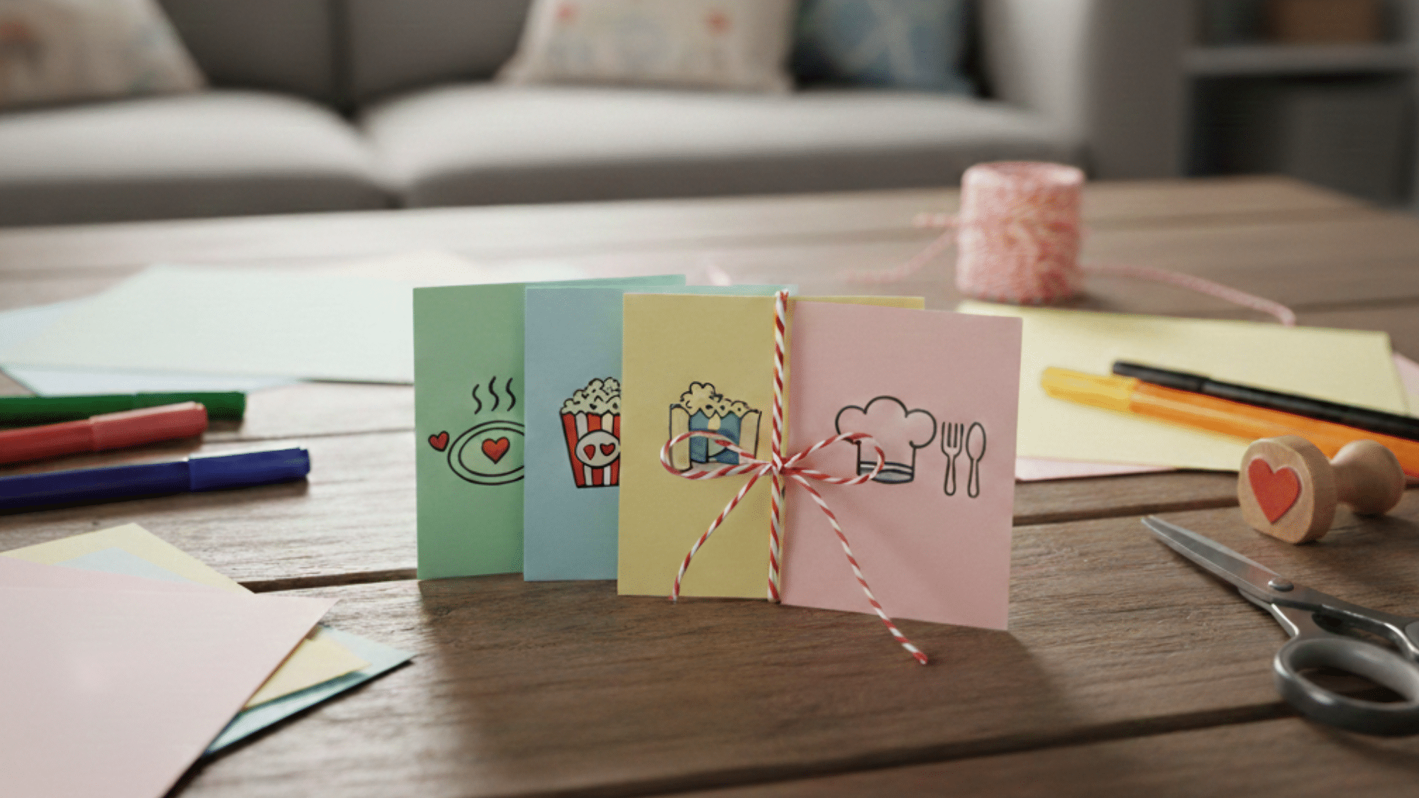 greeting cards with food-themed designs tied with twine, placed on a table with markers and scissors.