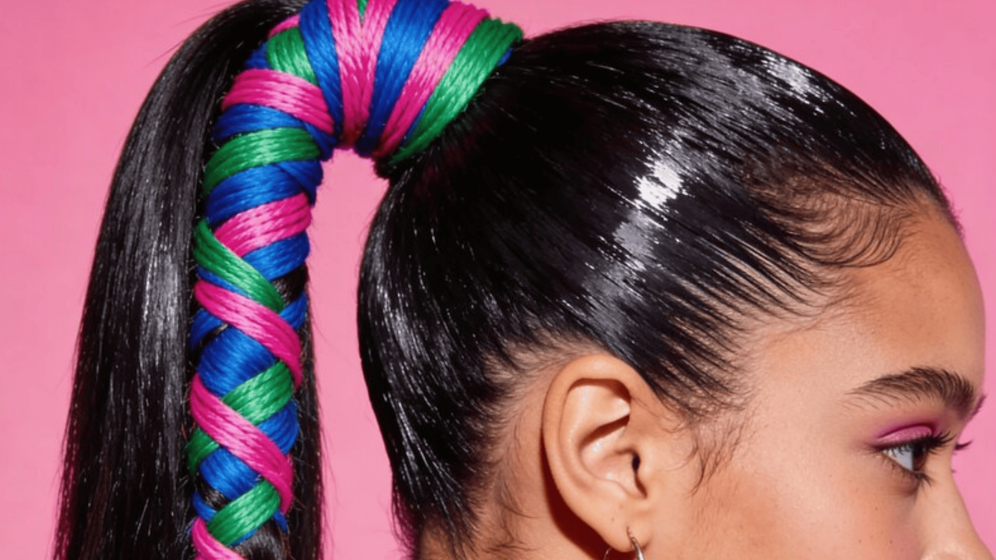 high ponytail wrapped with vibrant blue, green, and pink thread, creating a bold and colorful hairstyle against a pink background