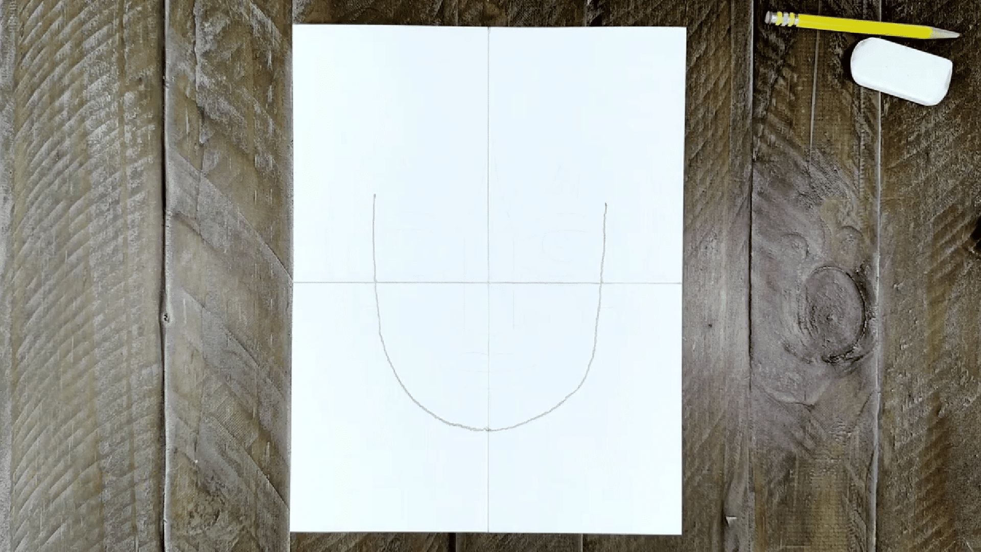 image shows a sketched outline of a face with guiding lines for symmetry, drawn on a piece of paper