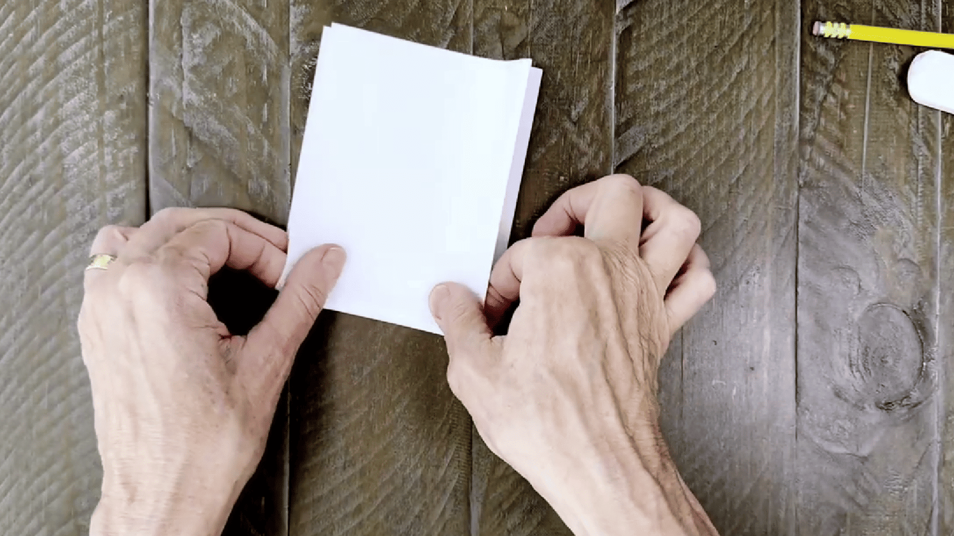 image shows someone folding a piece of paper in half in both directions to create creases.