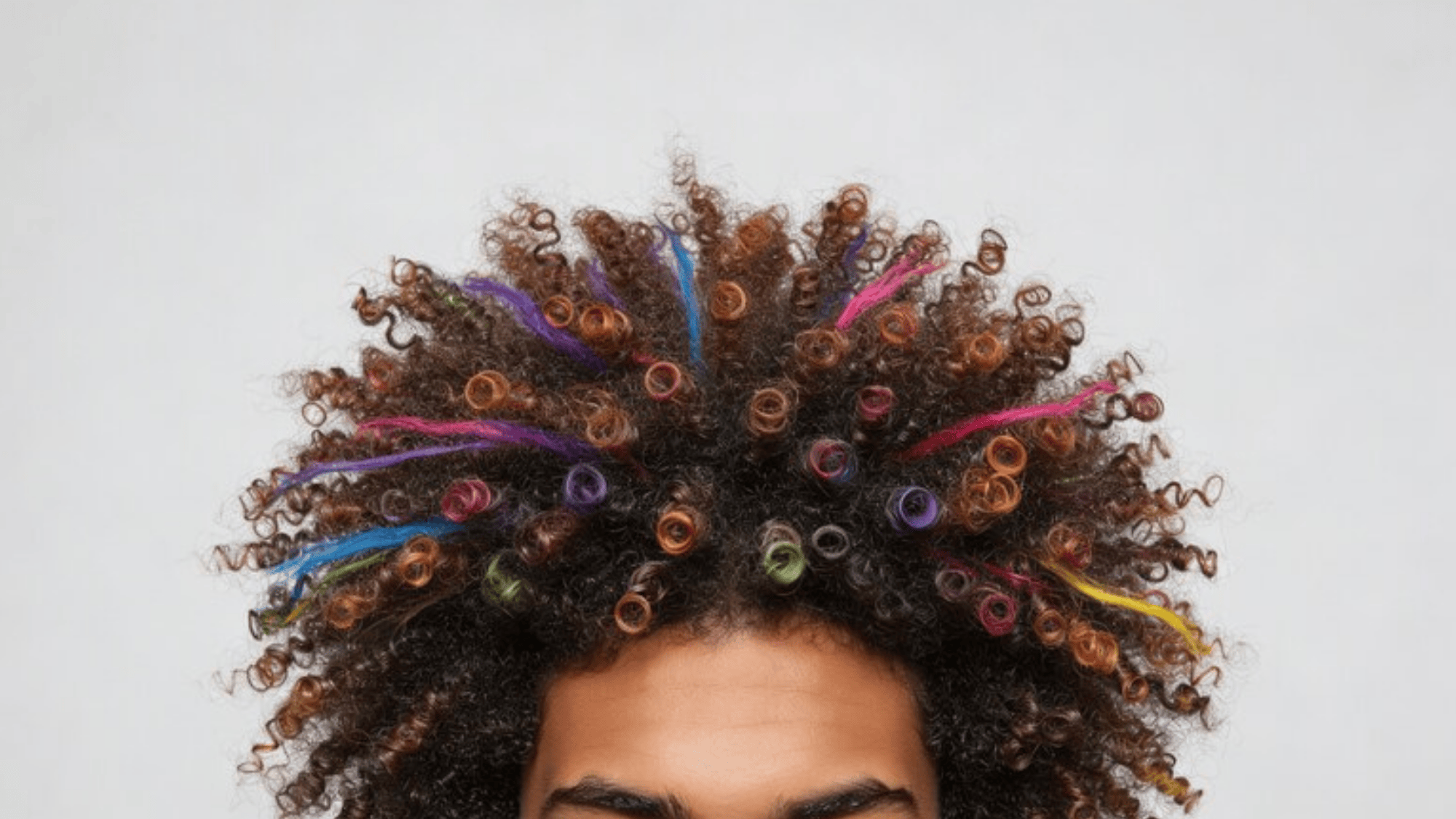 man with curly hair styled into vibrant, multi-colored ringlets, showcasing a playful and bold hairstyle