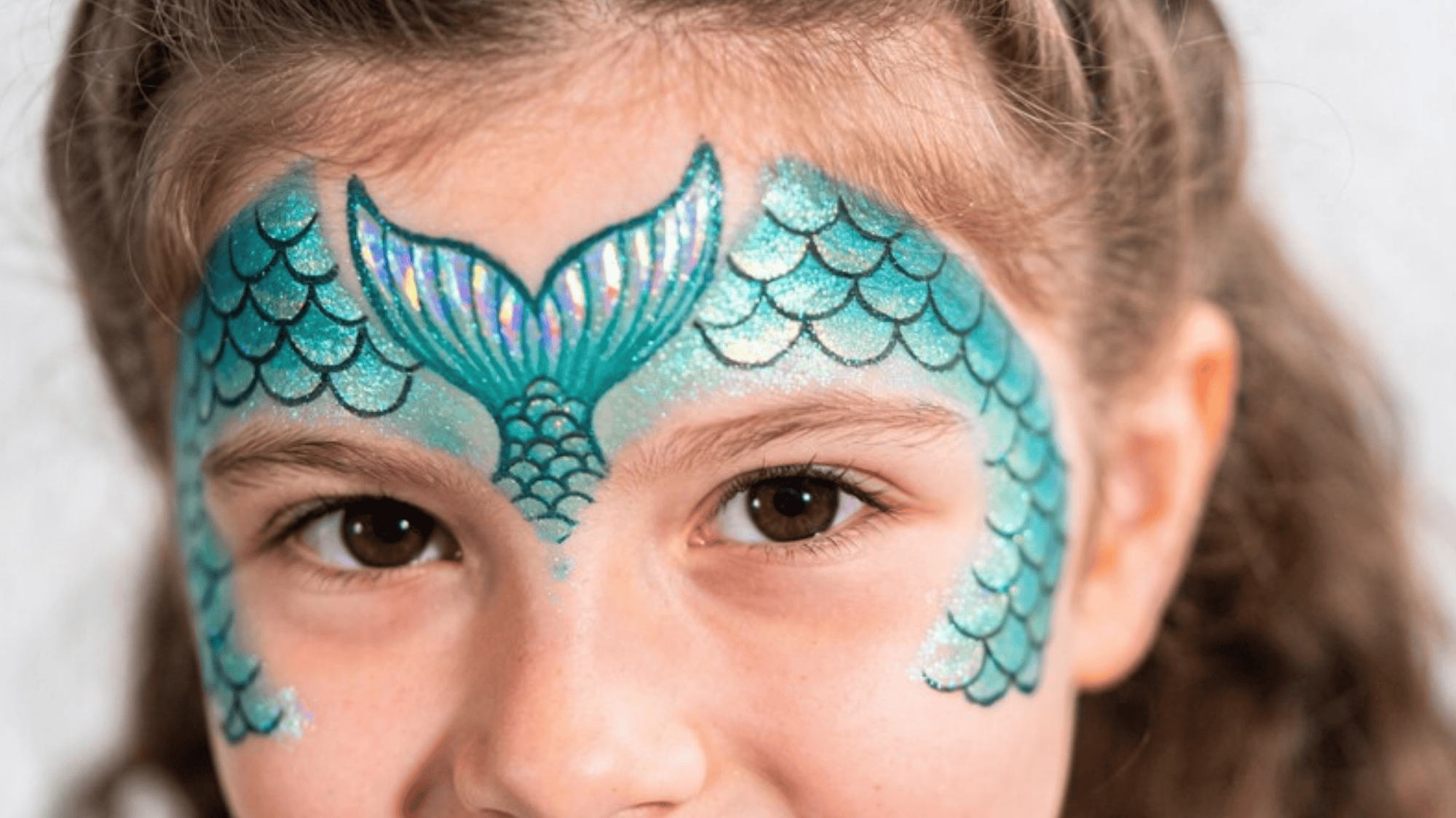 mermaid face paint on kid, shimmering teal scales across cheeks and forehead (1)