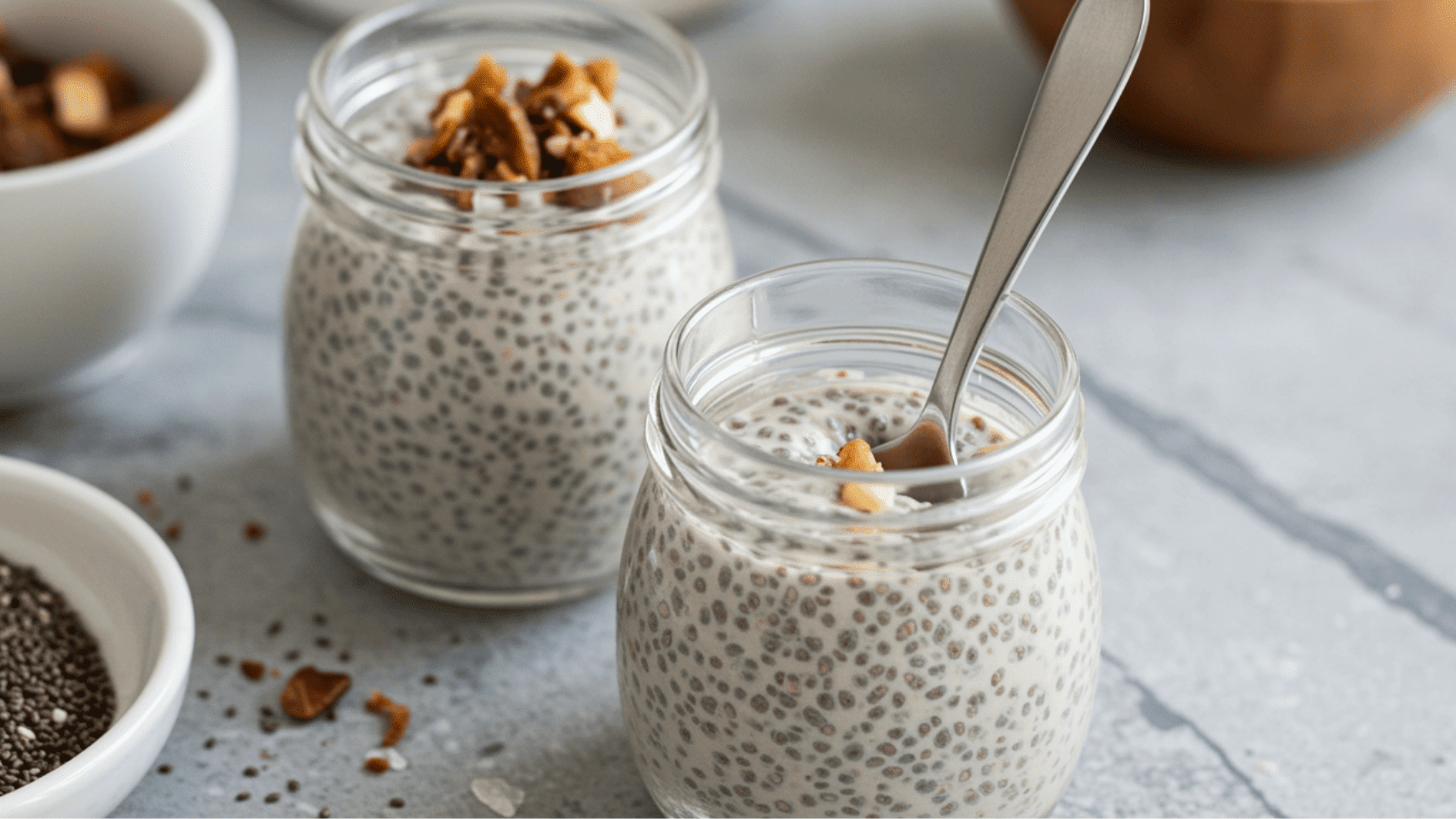 metal spoon placed inside a jar of thick coconut chia pudding topped with chopped nuts on a marble kitchen surface