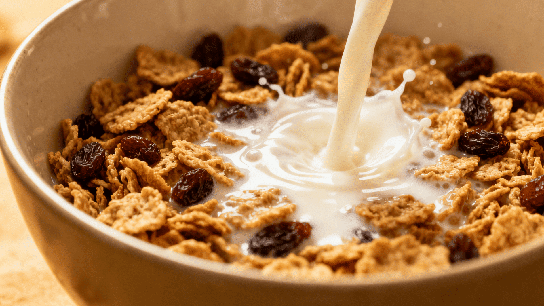 milk being poured into a bowl of cereal with raisins creating a splash in a breakfast bowl