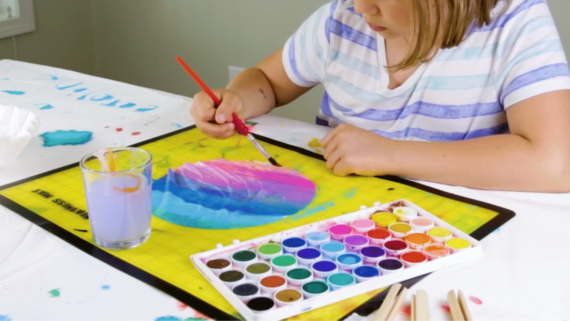 painting a coffee filter with a watercolor palette and paintbrush for controlled design.