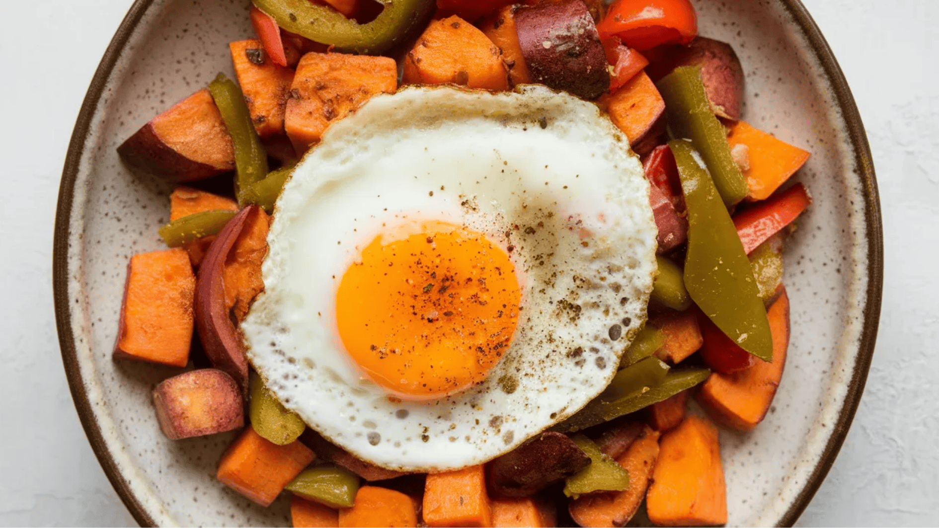 plate of roasted sweet potatoes, bell peppers, and jalapeños topped with a fried egg and seasoned with black pepper