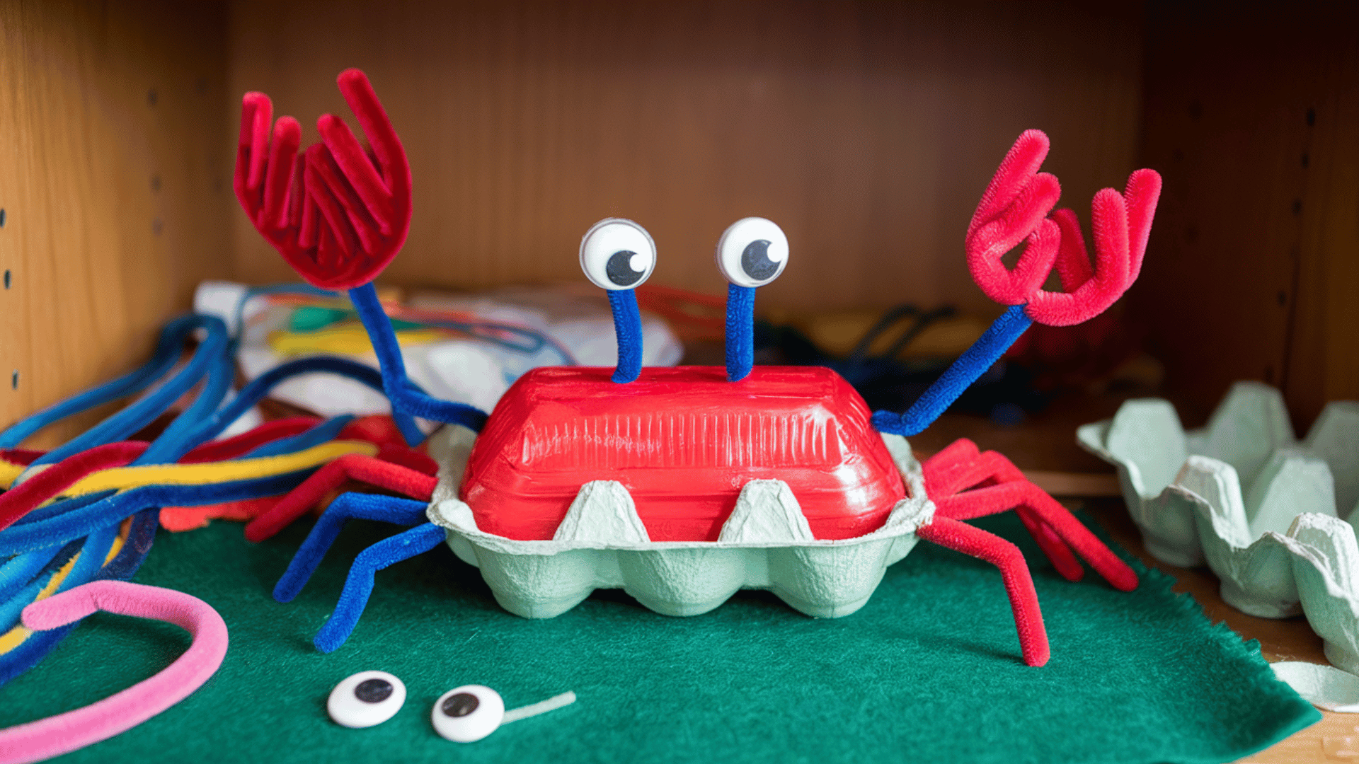 red-painted egg carton crab with googly eyes, pipe cleaner legs, pincers made from bent pipe cleaners