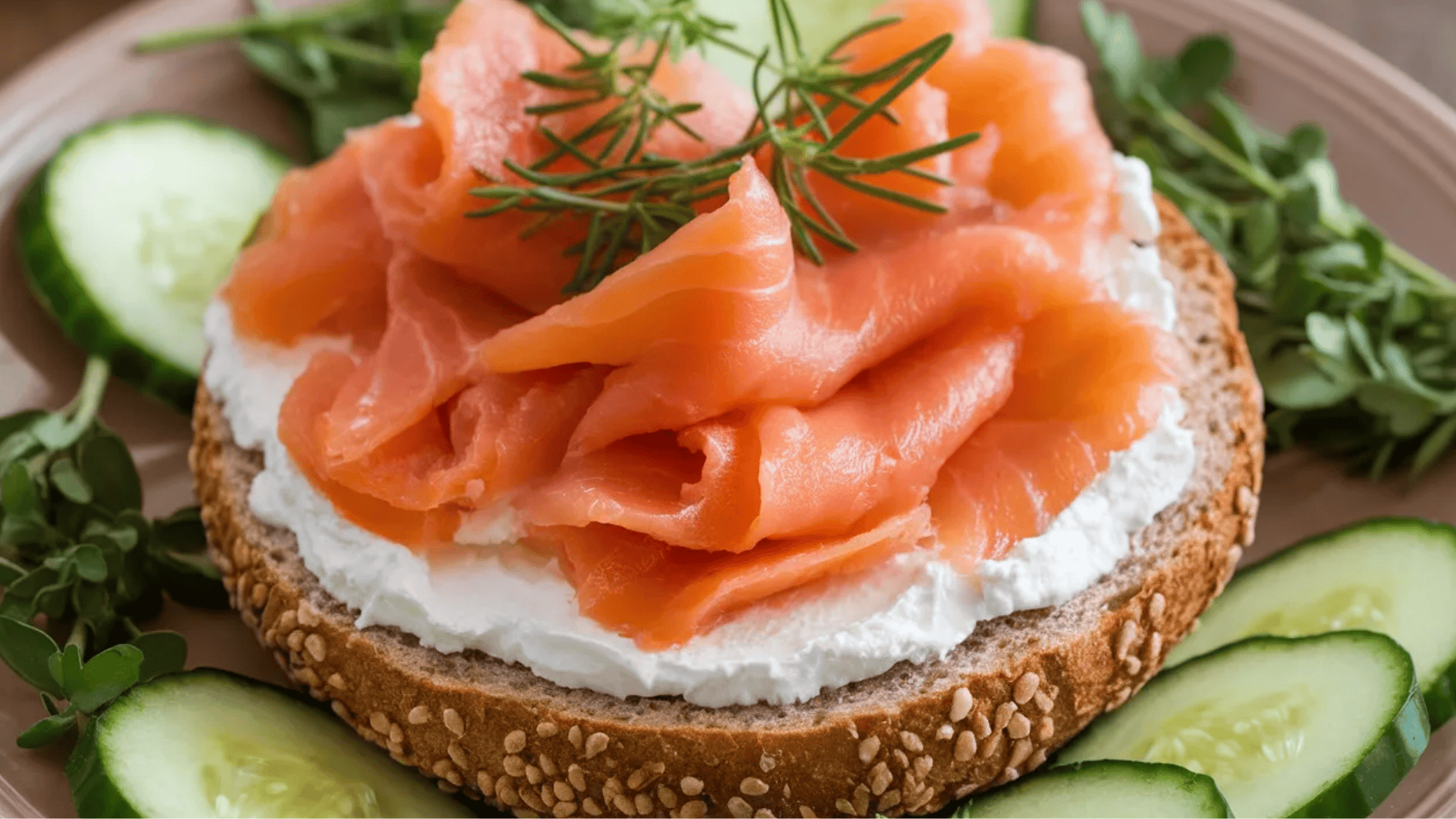 sesame seed bread topped with cream cheese, smoked salmon, fresh dill, and served with cucumber slices on the side