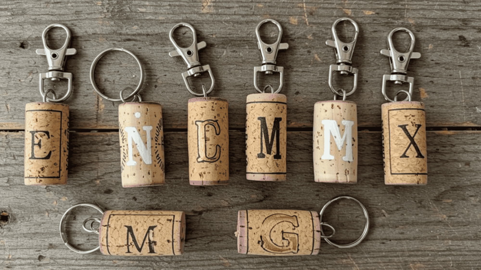 set of DIY wine cork keychains on a rustic wooden surface, each decorated with painted initials in gold and white, keyring hardware at the top