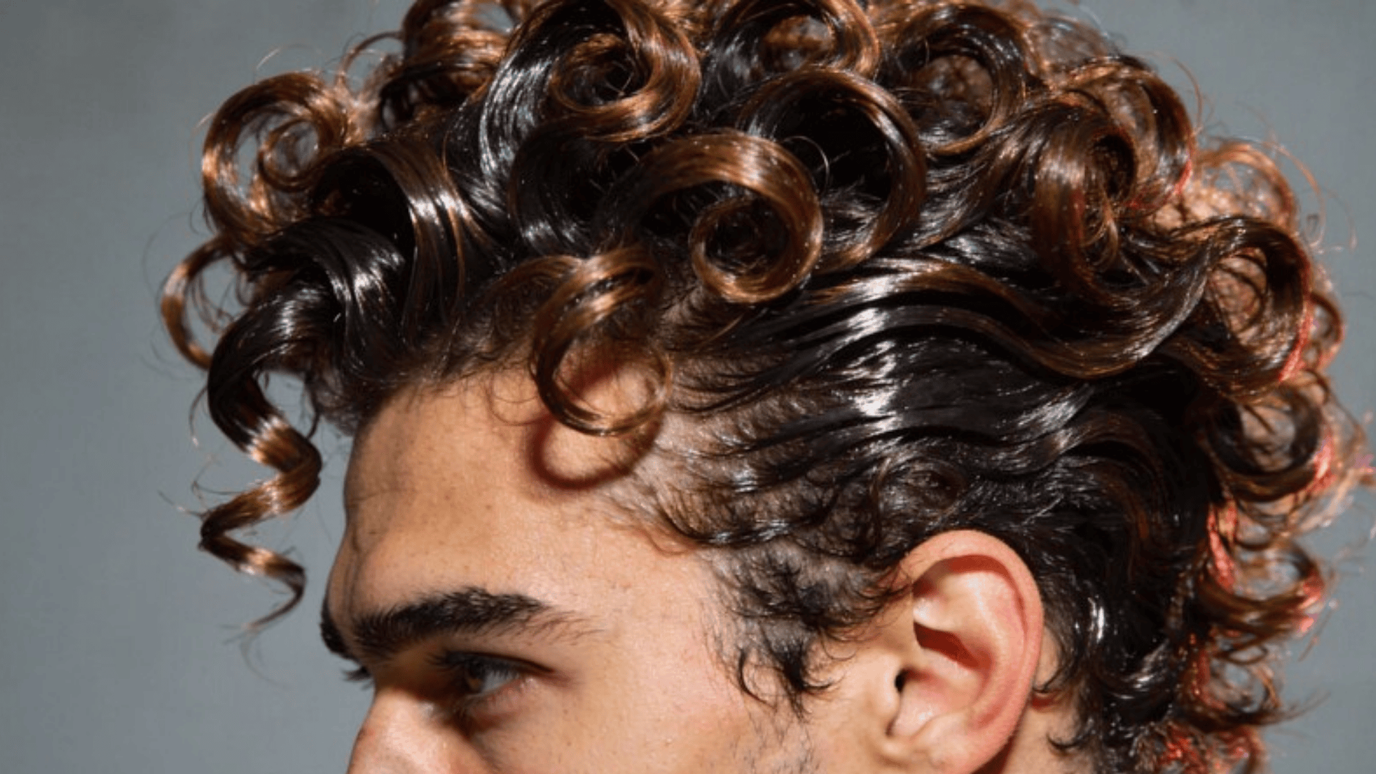 side view of a man with glossy, curly hair styled into defined ringlets, showcasing a voluminous and textured look