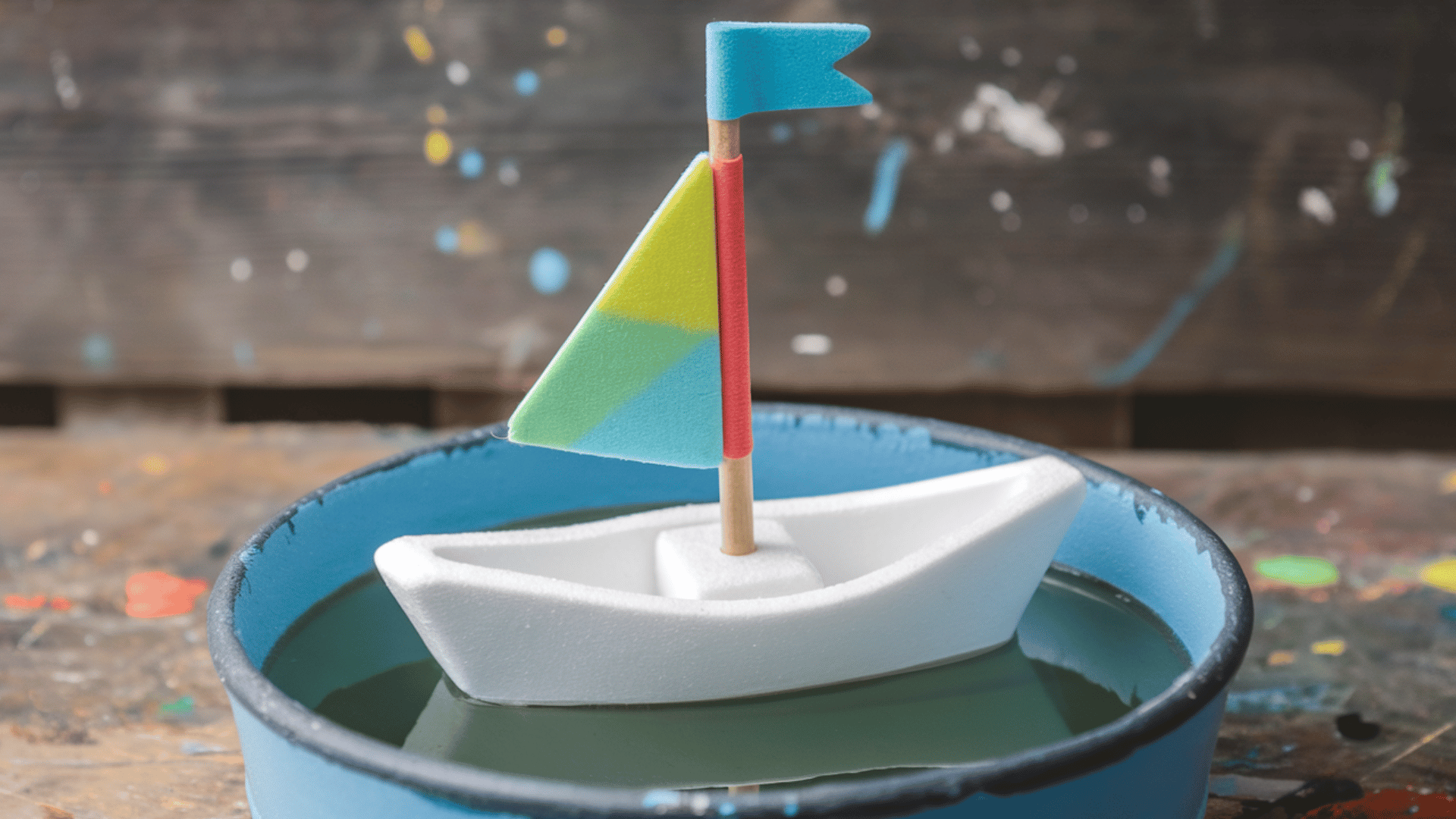 small foam boat with colorful triangular foam sail, wooden stick mast, tiny flag at the top