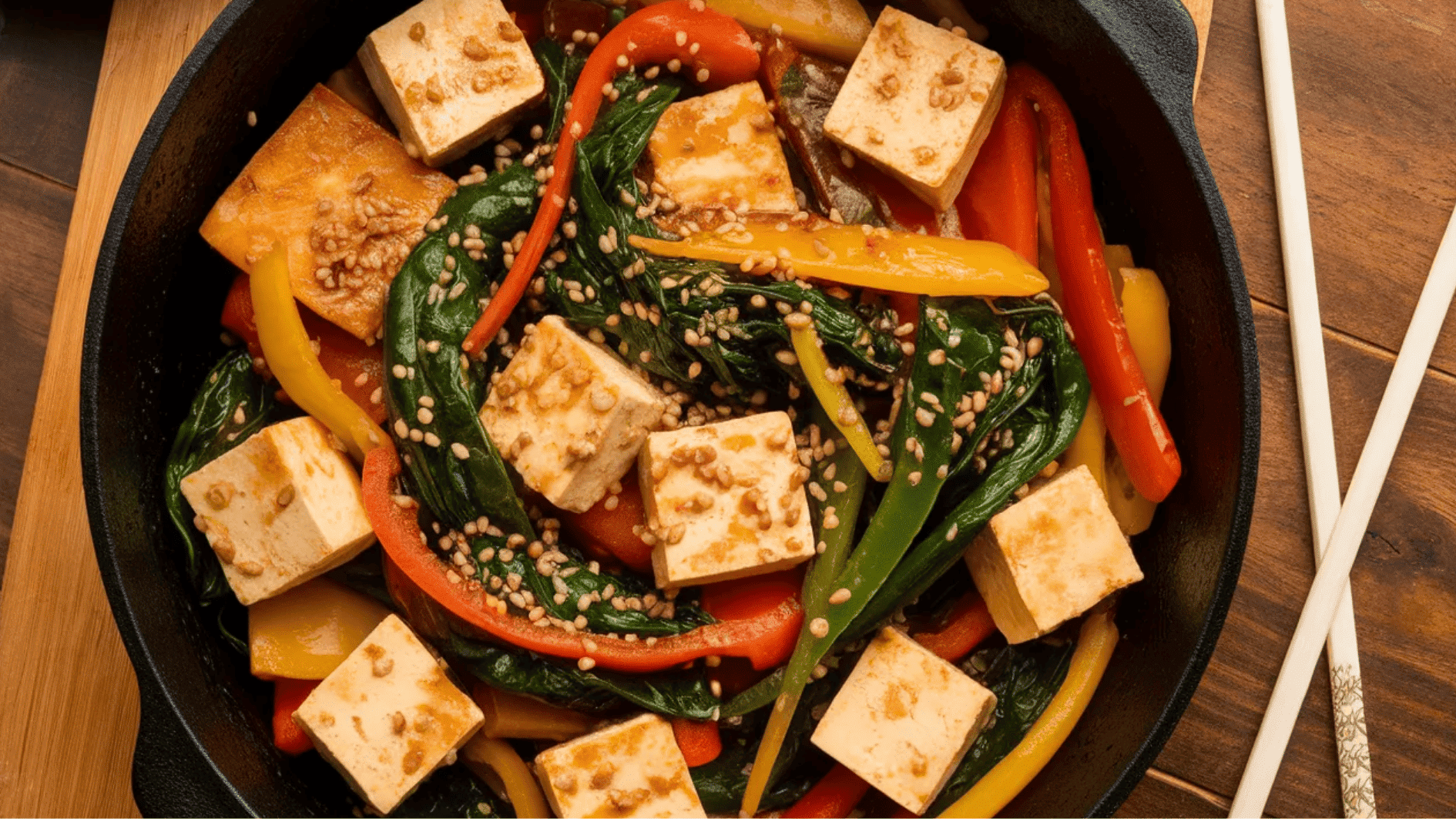 stir-fry dish with tofu, spinach, colorful bell peppers, and sesame seeds served in a black skillet