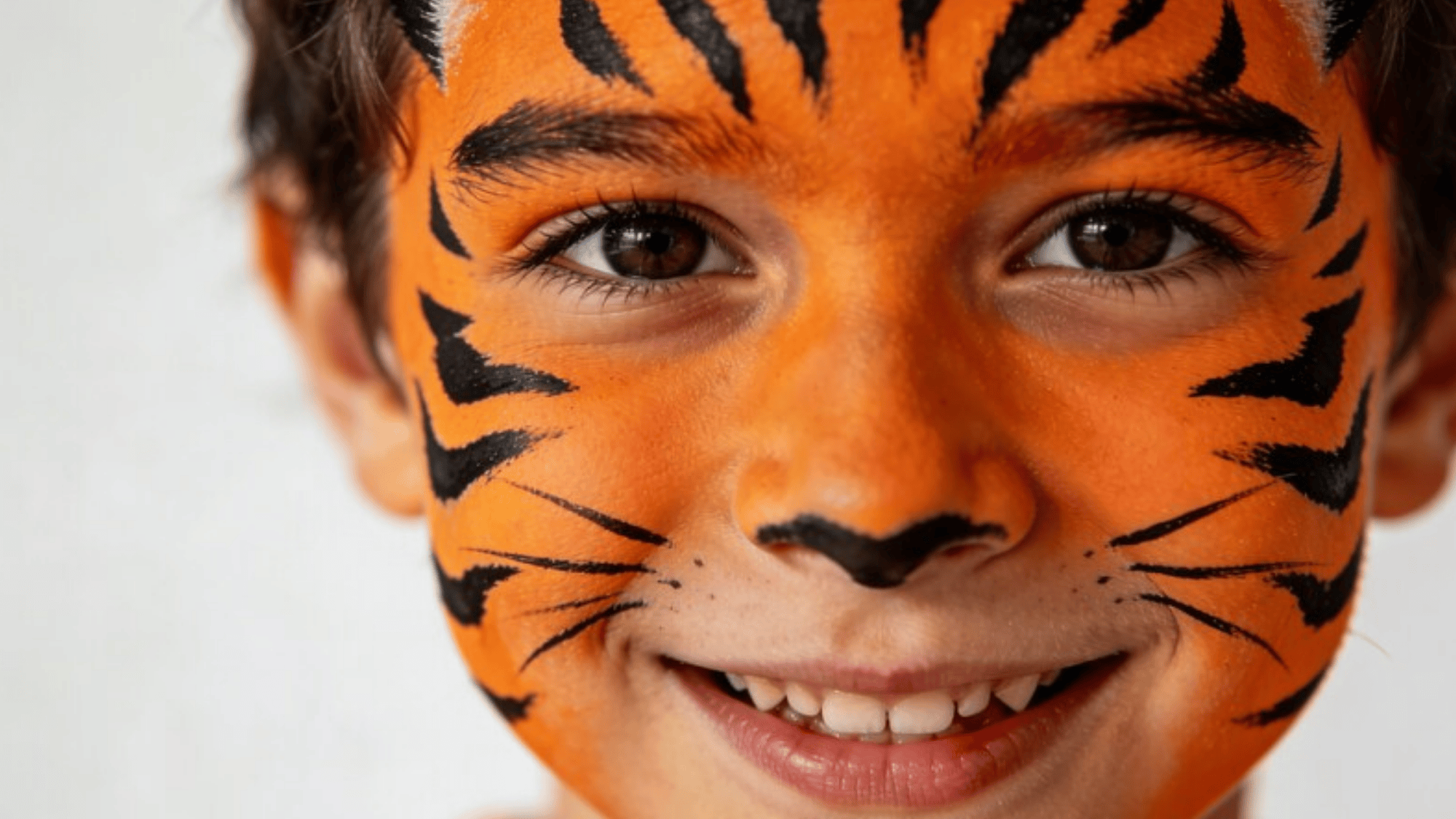 tiger face paint on kid, bright orange and black stripes, detailed whiskers, playful smile