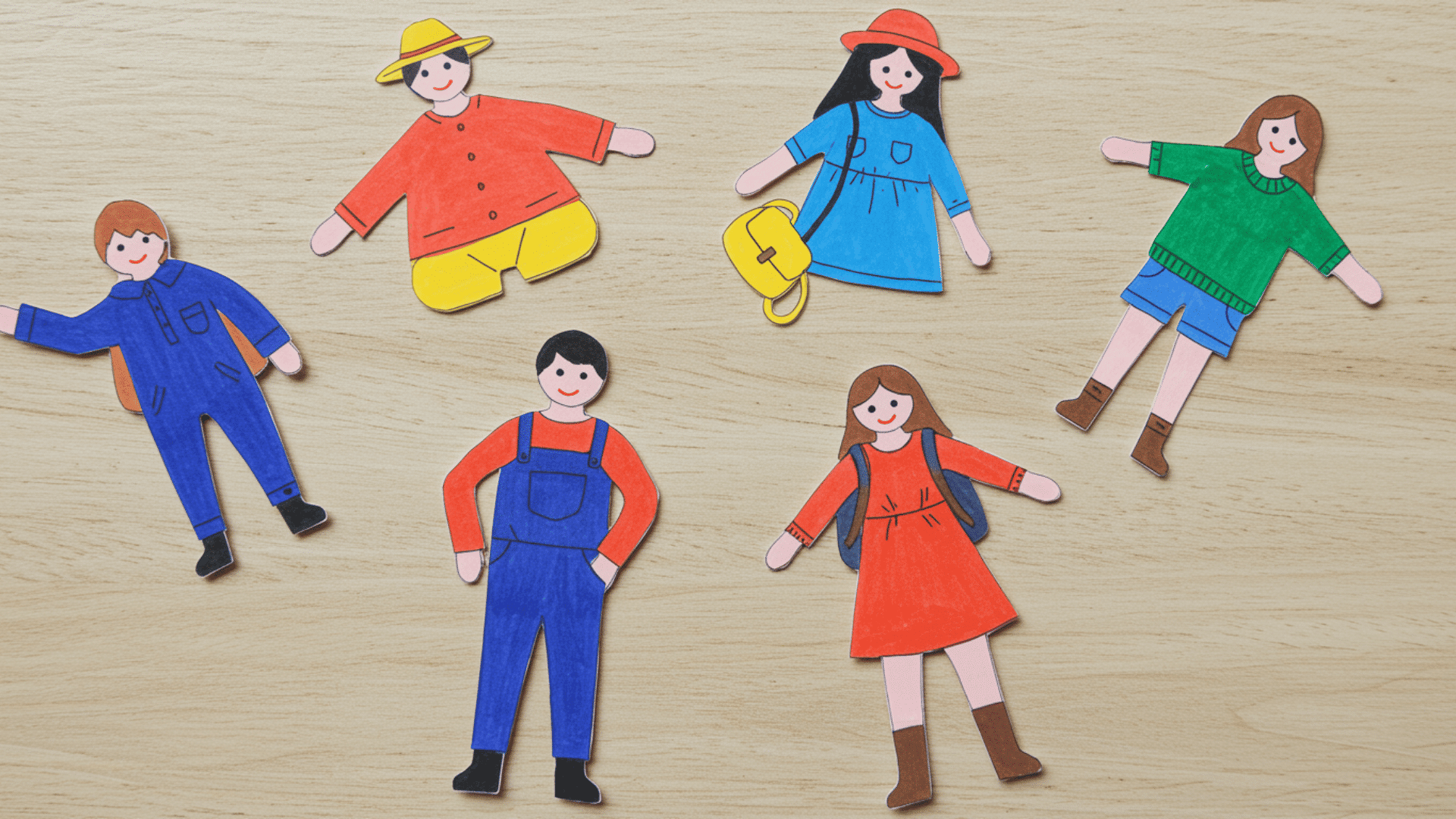 top-down view of a handmade family paper doll set showing parents and children in colorful everyday outfits on a wooden background.