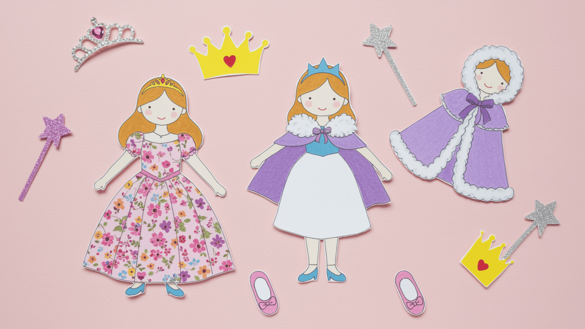 top-down view of handmade princess paper dolls wearing floral gowns, royal capes, and crowns, surrounded by tiaras, wands, and matching shoes on a pastel background.