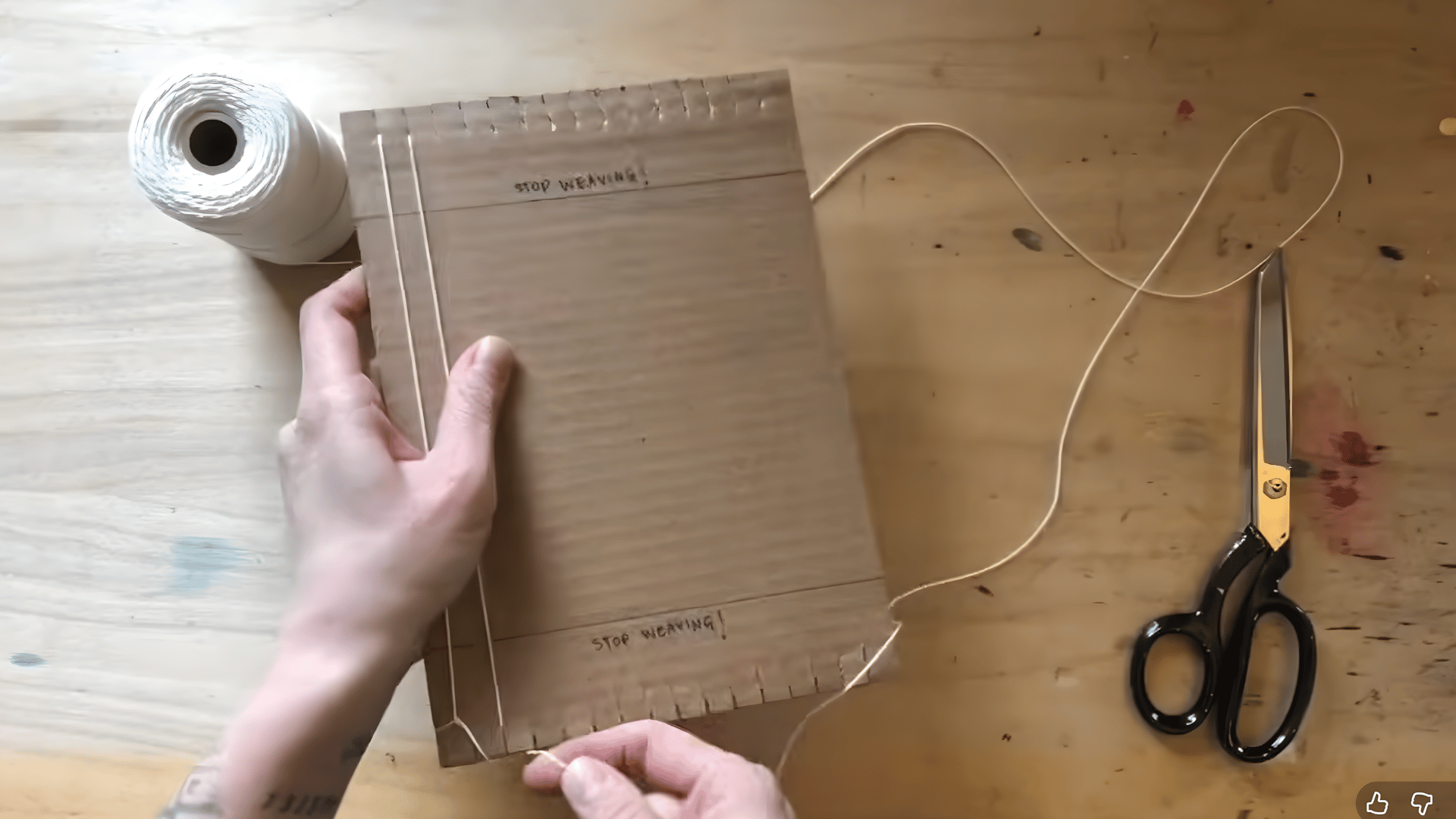 tying the warp thread to the first notch at the bottom of the cardboard loom to begin the weaving process