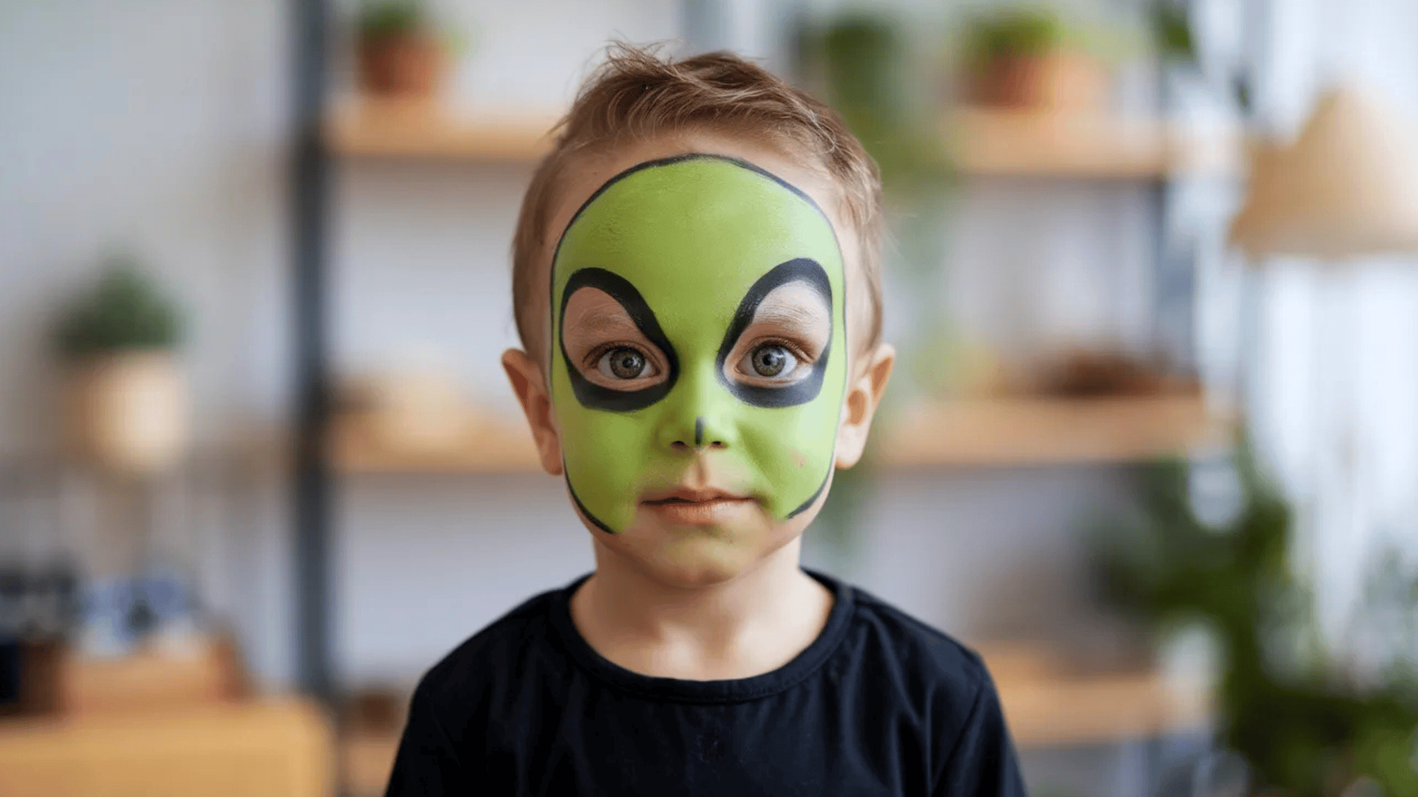 young boy with alien face paint, wearing a black shirt and standing in a bright room (1)
