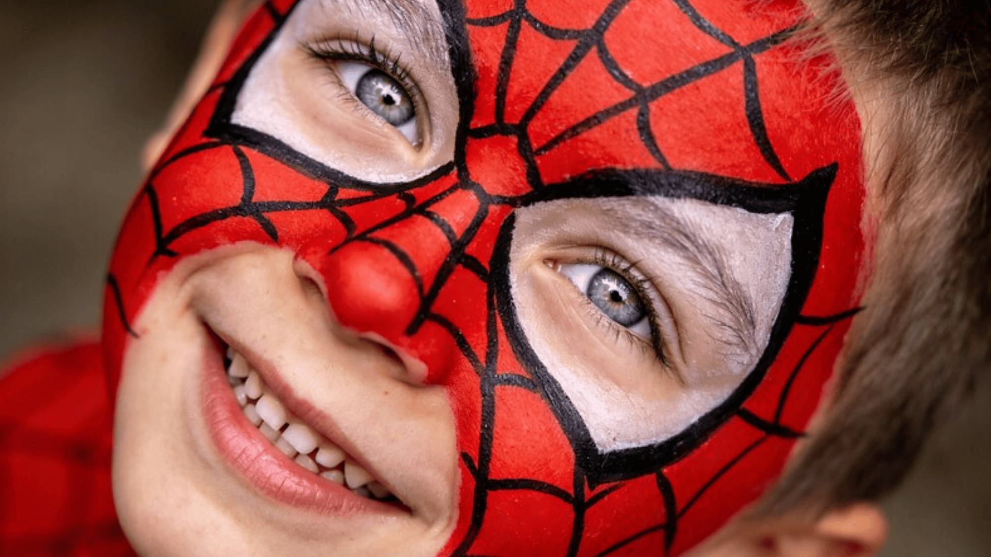 young child with Spider-Man face paint, bold red base, precise black web lines, playful expression